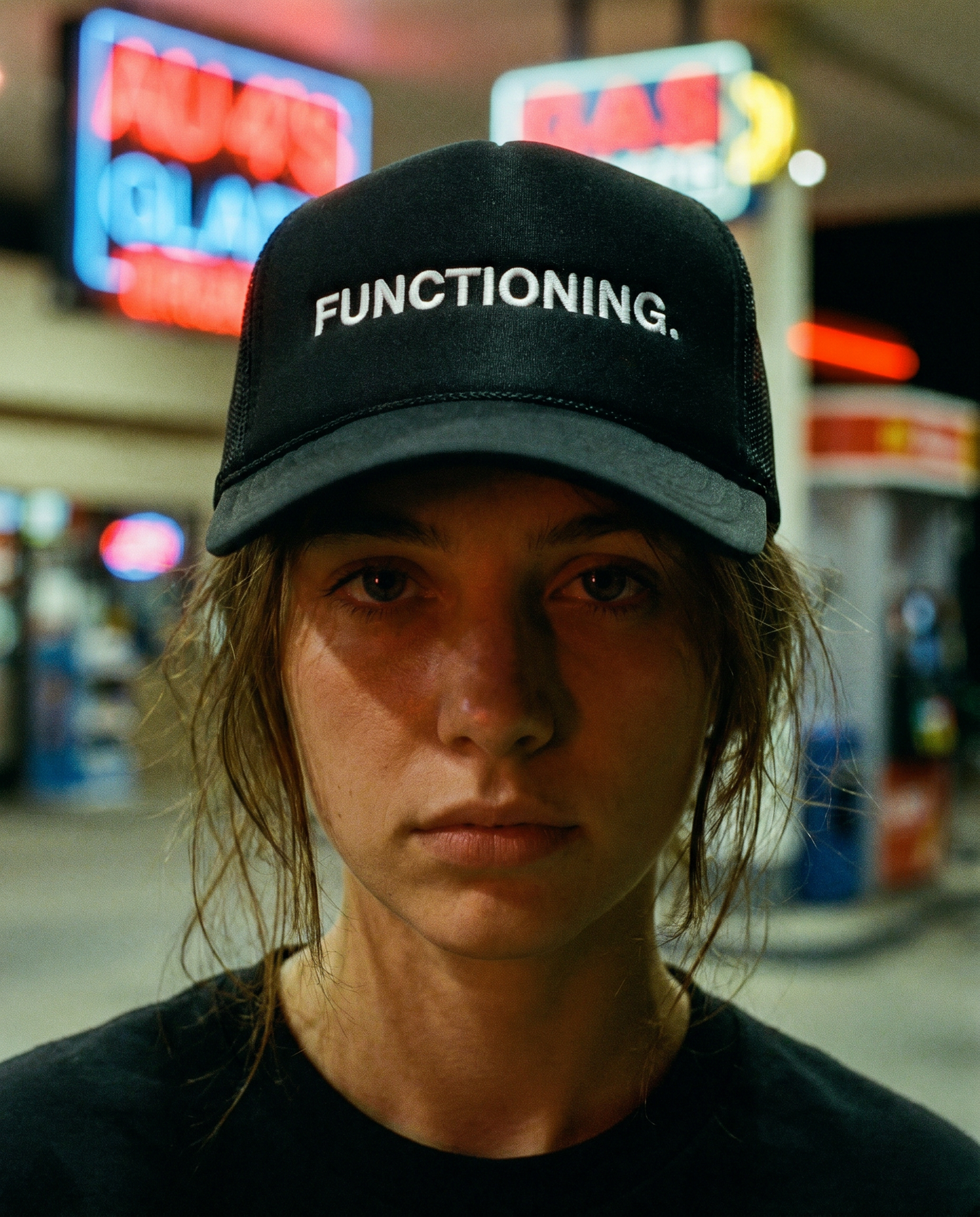 Person wearing a black cap with 'FUNCTIONING.' text in a gas station setting