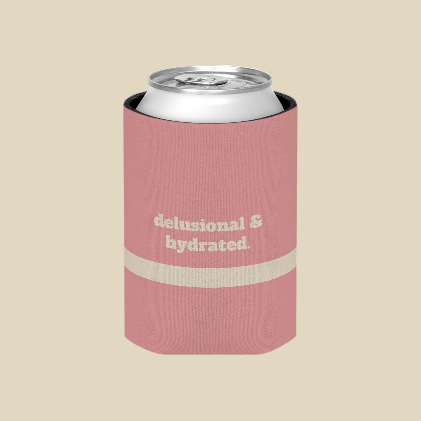 A pink can cooler sleeve holding a silver aluminum can, featuring the text 'delusional & hydrated.' in beige on the front, set against a plain white background.