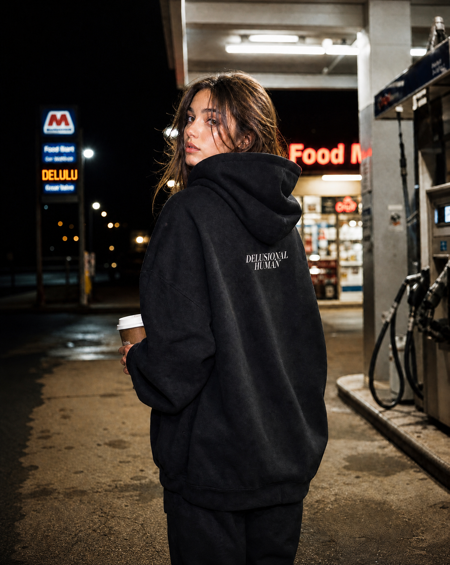 Person wearing a black hoodie with text at a gas station at night